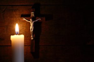 Small crucifix hanging on old wooden wall near lighting candle