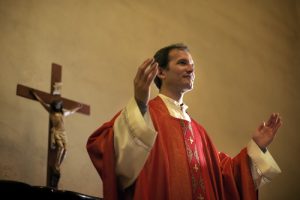 Catholic priest on altar praying with open arms during mass service in church