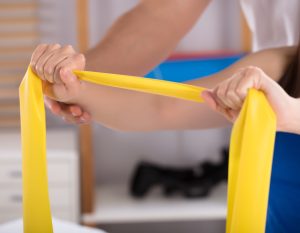 Physiotherapist Assisting Woman While Doing Exercise With Yellow Exercise Band