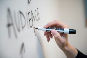 Person writing the word audience on a whiteboard